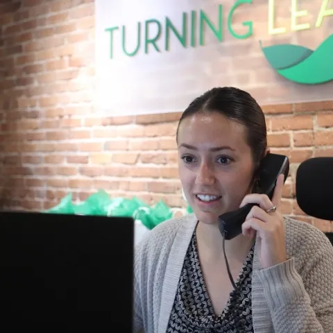 Front desk team member answering the phone beneath the Turning Leaf Dental sign