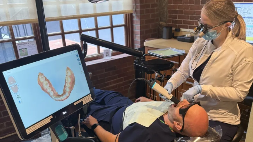 A dentist using the iTero scanner while the 3D scan of teeth shows on screen
